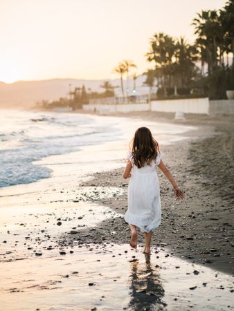 Adorable girl walking on seaside at sunset