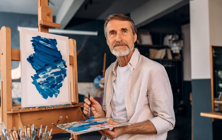 Male artist in his studio with blue painting on easel