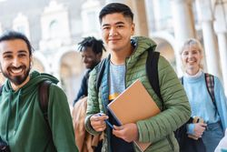 Group of diverse students with books and backpacks happily walking through campus