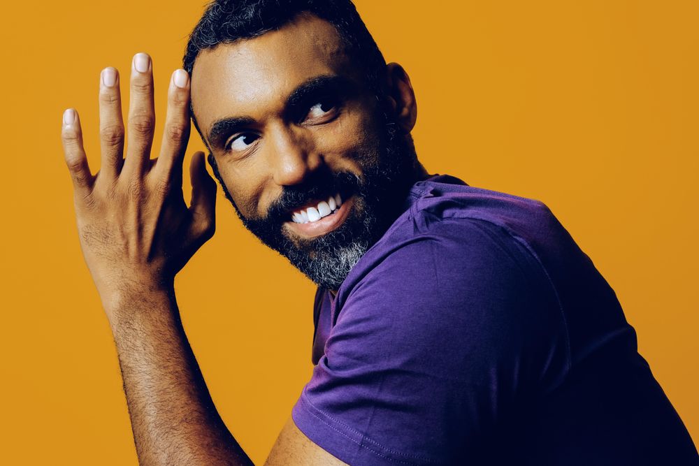 Confident Black man in yellow studio smiling with hand on to his face