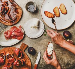 Crostinis with prosciutto, goat cheese and grilled figs, with hands spreading cheese