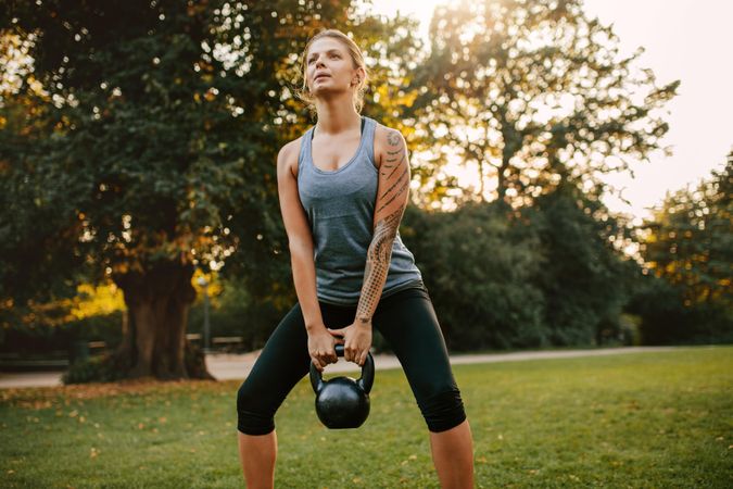 Portrait of strong young woman exercising with kettlebell weights in the park
