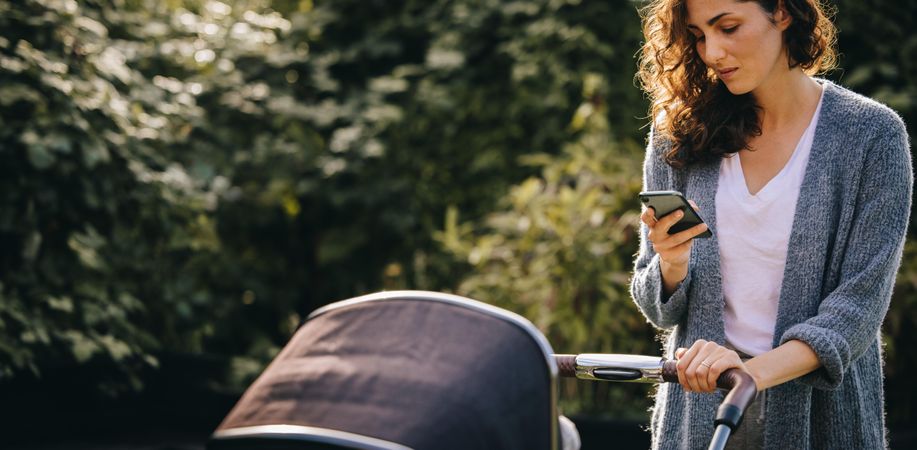 Woman checking messages on her smart phone while pushing an infant stroller