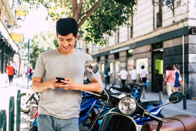 Confident Asian man talking on phone while standing by motorbike