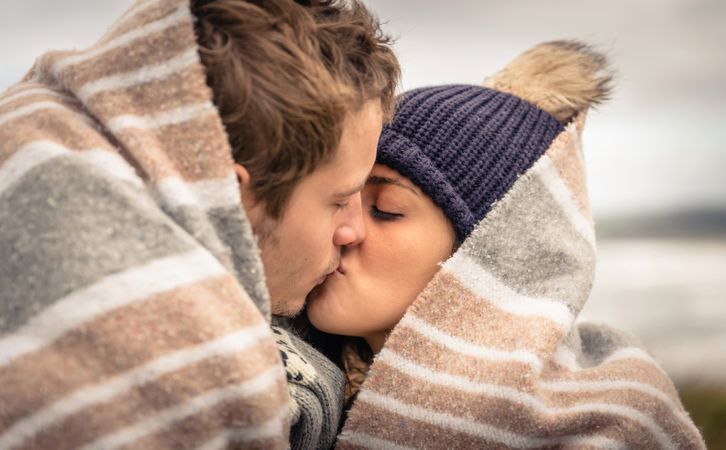 Close up of couple cuddling while wrapped in blanket on a windy day