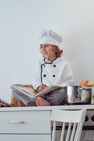 Preteen boy sitting with opened culinary book on kitchen table