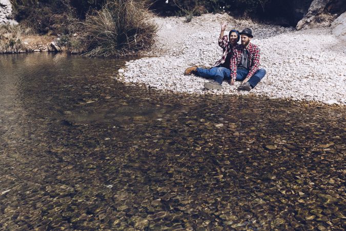 Positive woman and man resting on stone shore near river