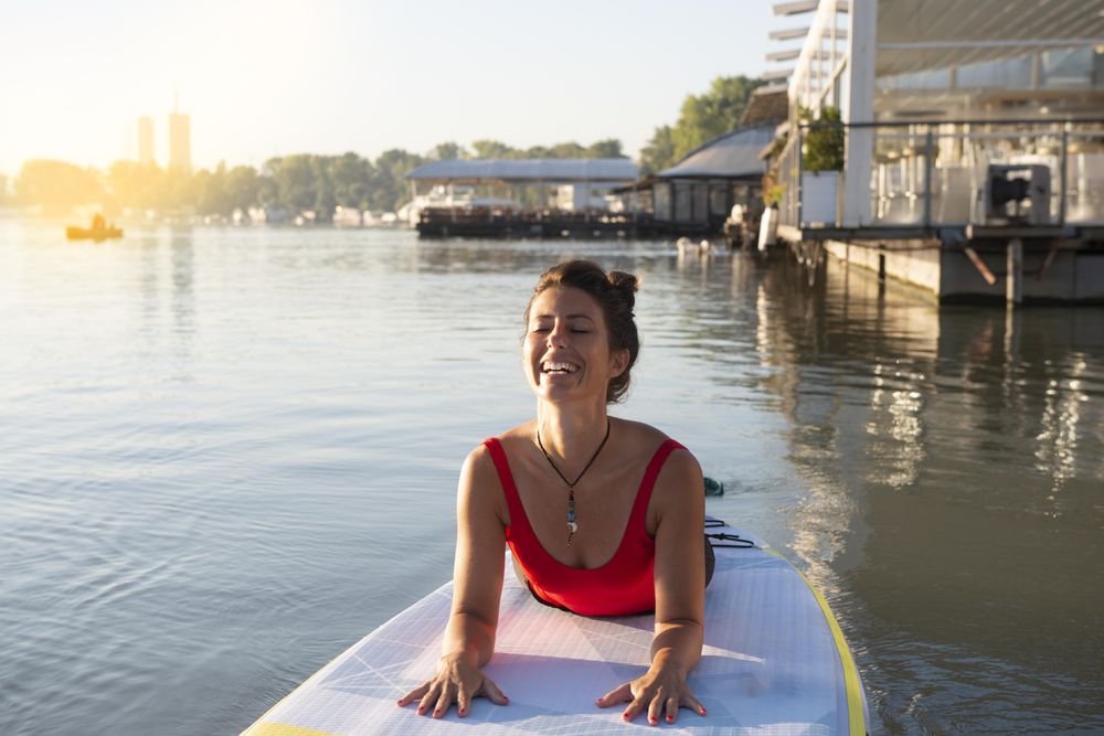 Smiling woman stretching back on paddleboard in lake in pier