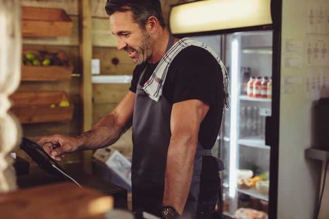 Waiter in apron using cash register to take customer’s payment