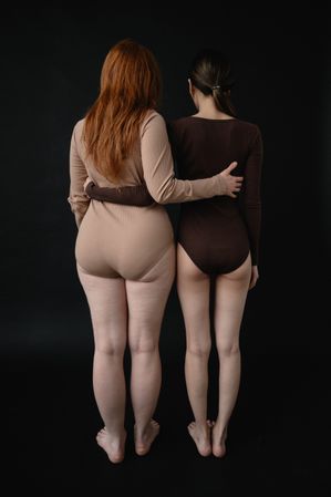 Back view of two woman in leotard standing against dark background