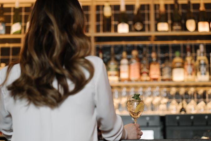 Back view of anonymous woman holding a cocktail in bar