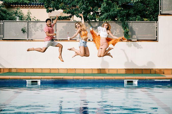 two young women and a man jumping by the pool
