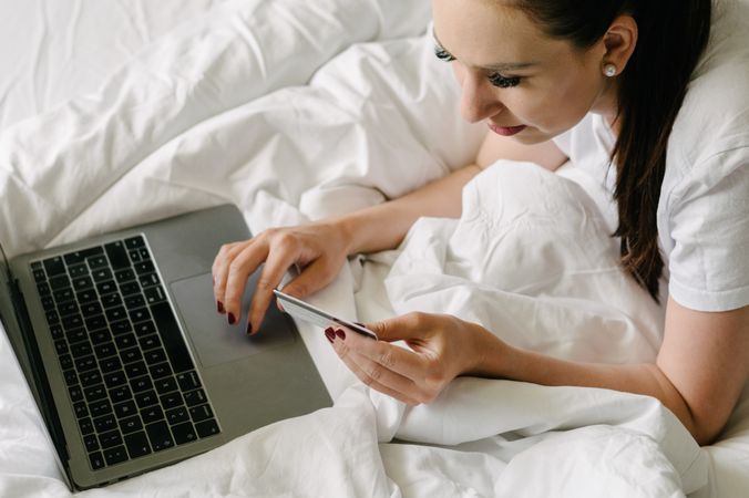 Crop woman using tablet while shopping on bed