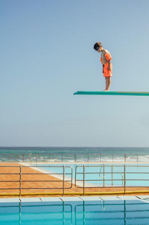 Boy learning to dive from diving platform at outdoor swimming pool