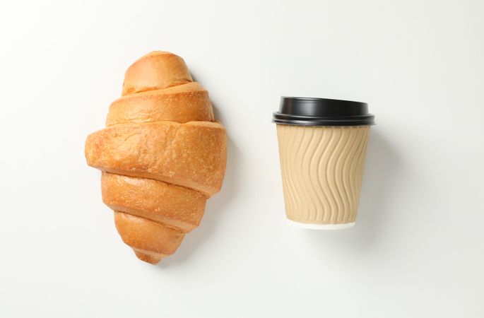 Flat lay of croissant and cup of coffee on plain background