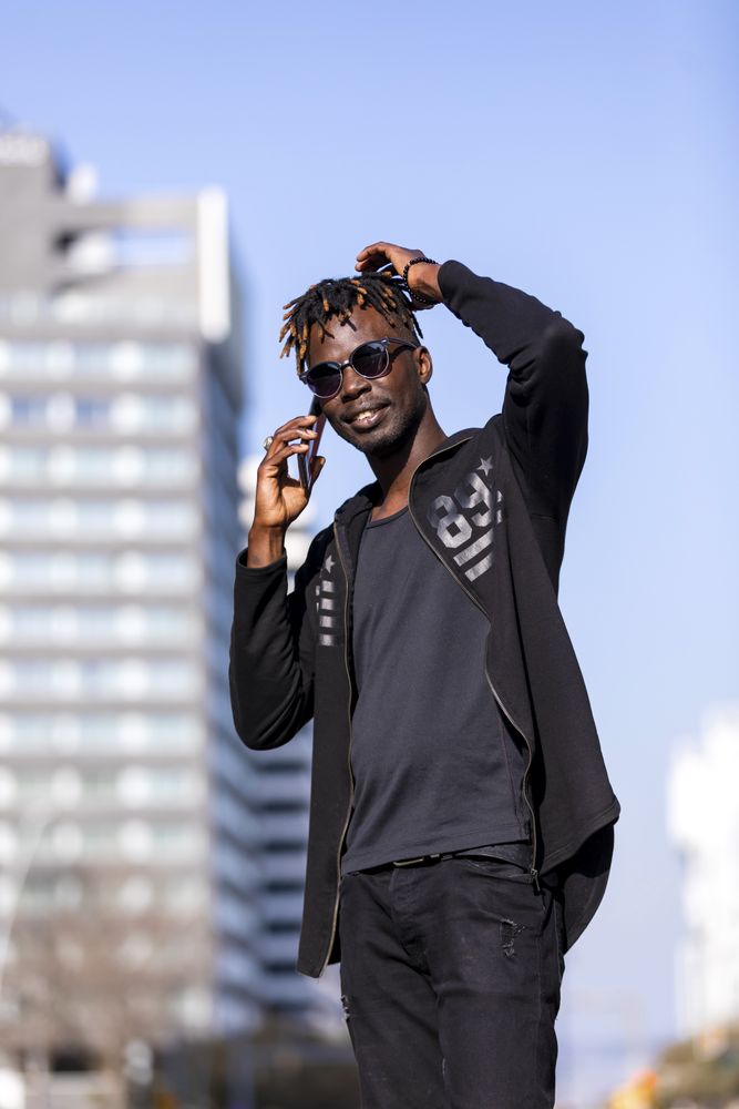 Front view of Black male with sunglasses standing against cityscape on the street while using a mobile phone in sunny day