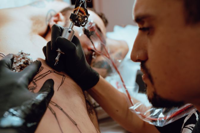 Man using tattoo gun on client's ribs