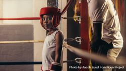 Girl wearing boxing gloves and headgear standing in a corner of a boxing ring 0JovK5