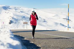 Young woman enjoying running on road in winter clothes