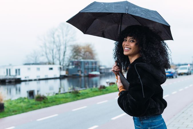 Smiling Black woman with umbrella on street