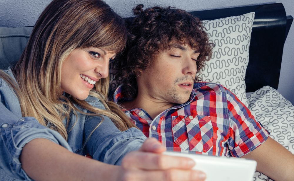 Woman taking photo of man sleeping in bed