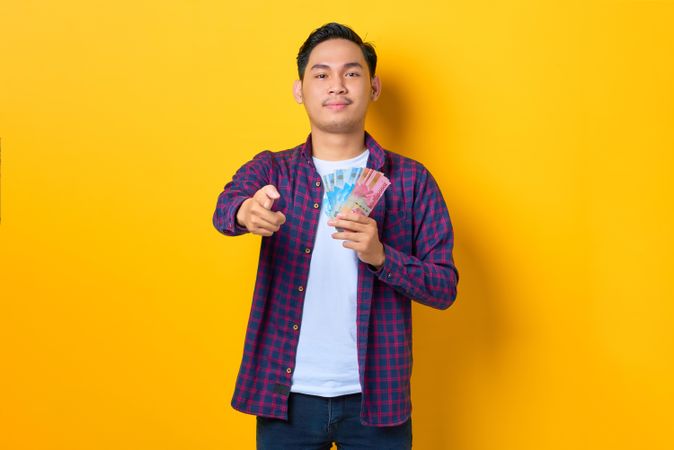 Young Asian man in plaid shirt  pointing while holding banknotes