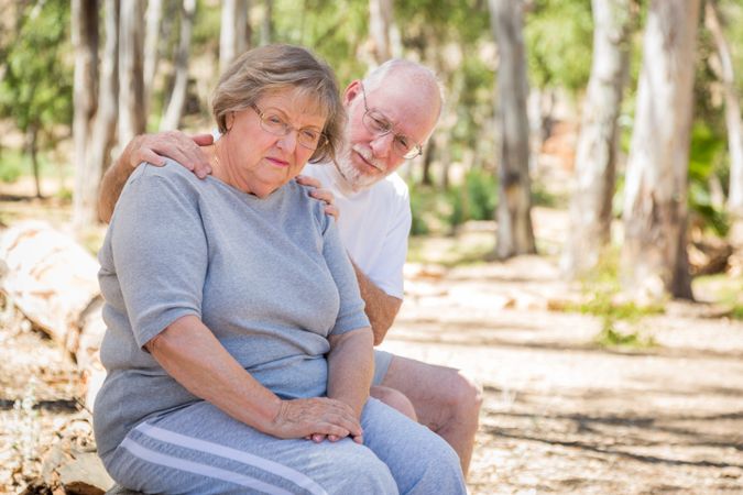 Upset Mature Woman Sits With Concerned Husband Outdoors