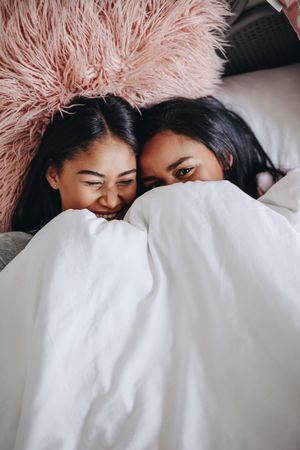 Two young friends laughing lying on bed during a sleepover