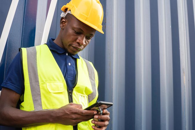 Portrait of Black male factory worker in safety uniform checking phone