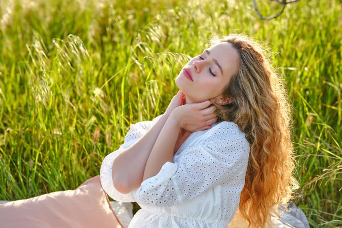 Wman touching neck tenderly on grassy meadow