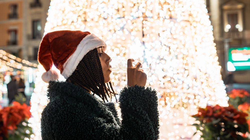 Young woman in a Santa hat drinking champagne in front of a Christmas tree.