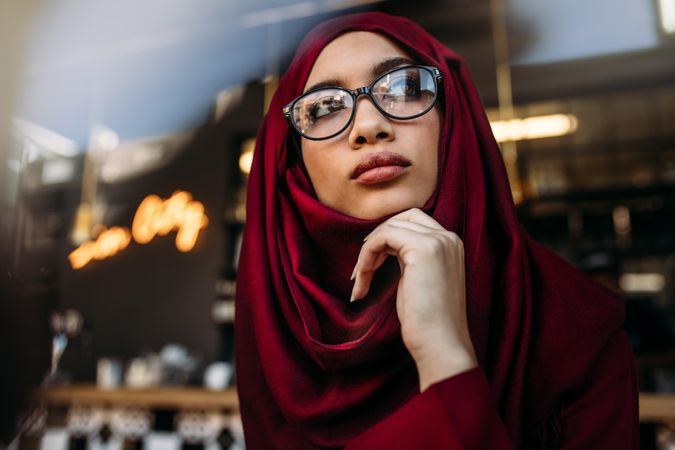 Muslim woman in hijab and eyeglasses looking away with hand on chin