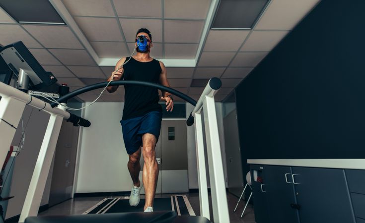 Male athlete with mask running on treadmill to analyze his fitness performance