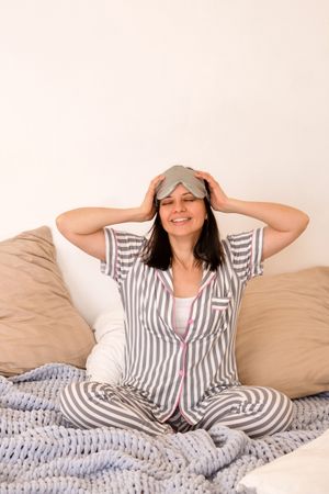 Woman adjusting eye mask, smiling in bed.