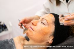 Side view of cosmetologist brushing product on client's chin 0gX9Ke