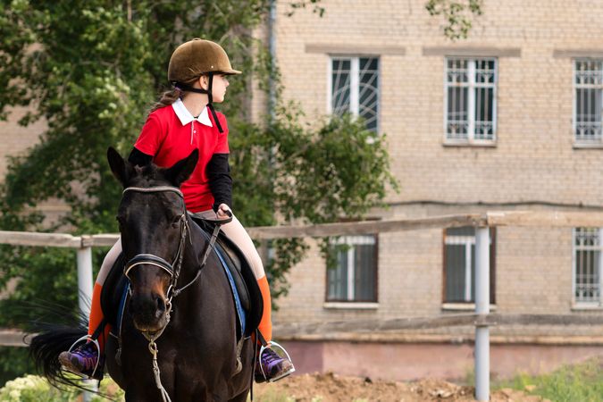 Young rider on horseback looking sideways at stables.
