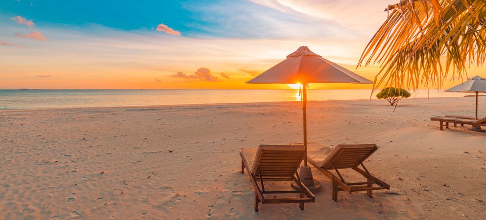 Wide shot of a colorful sunset on deserted beach with two lounge chairs