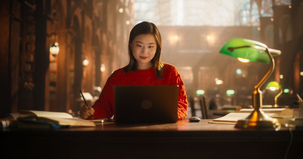 Dedicated Asian Female Student Engaged in E-Learning with Laptop in Classical Library.