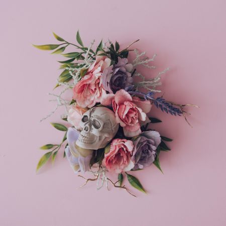Plastic skull within a flower arrangement on a pastel pink background
