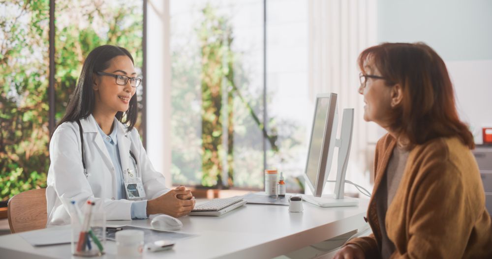 Asian Female Doctor Speaking to a Mature Woman During a Consultation in Health Clinic.