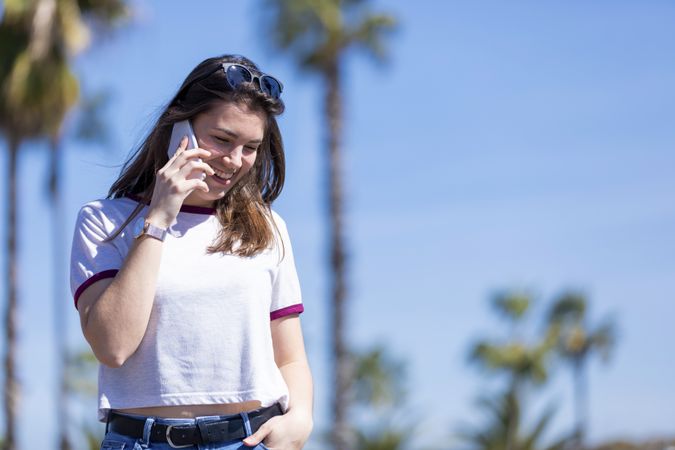 Coy woman wearing clothes standing outdoors in the street while using a mobile phone on a sunny day