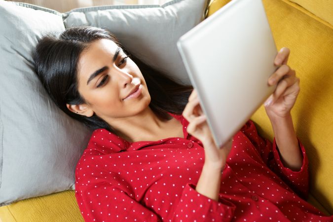 Woman lying back on sofa while reading a tablet