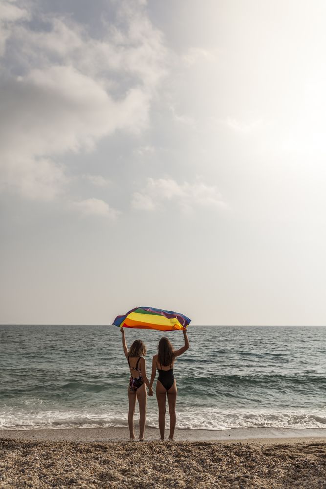 Females standing with rainbow flag on seashore