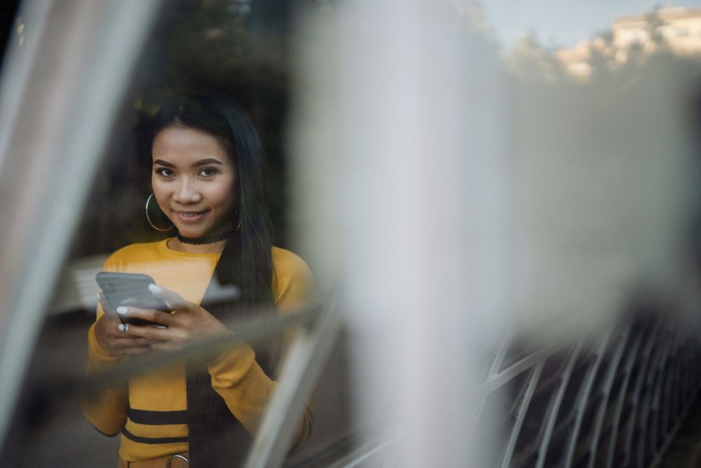 Charming Asian woman browsing smartphone and looking at camera