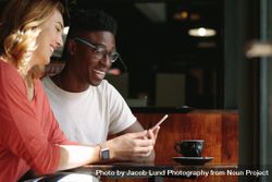 Man and woman sitting at a coffee table looking at a mobile phone 49rxab