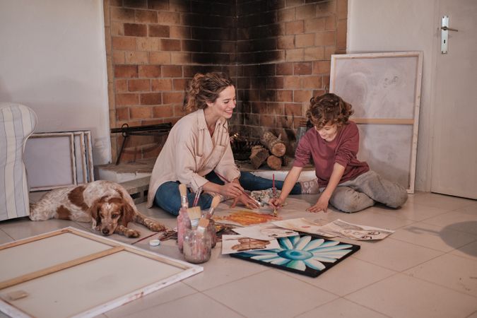 Positive woman teaching boy to create picture with paints