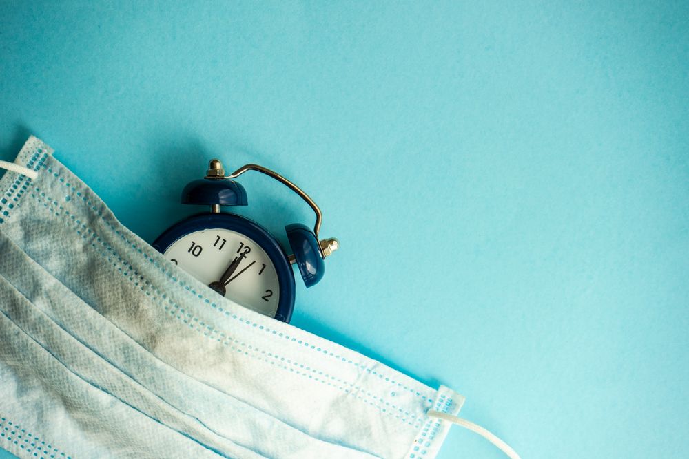 Clock and facemask on blue pastel background with copy space
