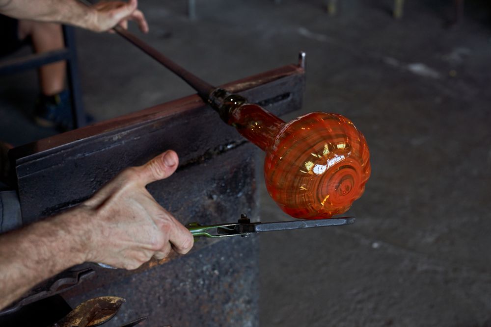 Crop gaffer shaping melted glass in dark workroom