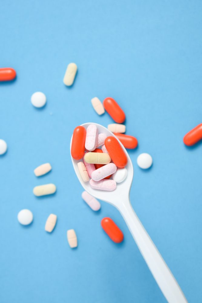 Plastic spoon with various colorful pills on blue table