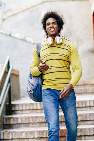 Man in yellow shirt and headphones walking down stairs outside